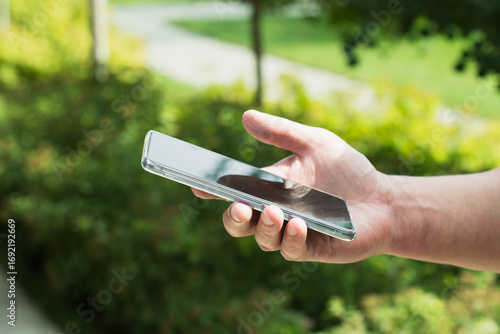 Close-up of a hand holding a smartphone outdoors on a sunny day.