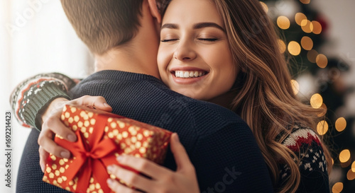 Woman hugging man while holding christmas gift with christmas tree lights in the background