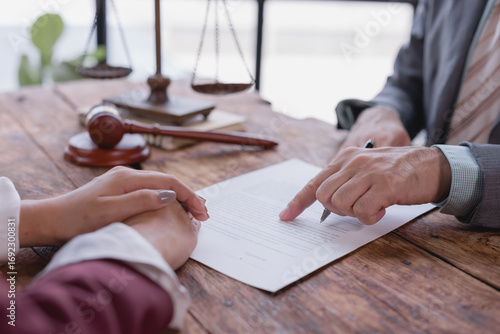 Lawyer presenting key sections of a contract document to client during a legal consultation in an office, featuring scales of justice and a gavel on the table