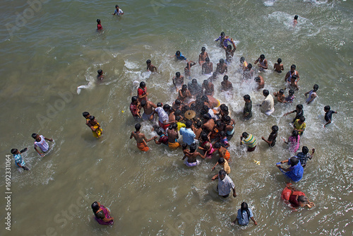 Puducherry, India - 28 February 2010: Aerial view of a lively scene where people gather and frolic in the ocean's embrace, creating a vibrant contrast against the sandy shore.