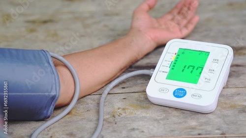 Close-up of a person measuring blood pressure with an automatic digital monitor on a wooden table, showing systolic, diastolic, and pulse readings for health check and medical care concepts.