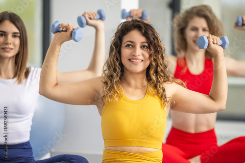 Women exercising with dumbbells in a fitness class during daylight in a modern gym setting