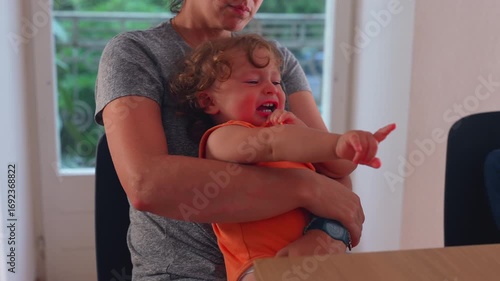 Mother Holding Crying Baby Pointing Toward Table While Comforting Child in Domestic Home Setting During Emotional Moment