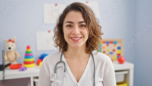 A friendly portrait of a female pediatrician in a children's clinic. She is smiling and wearing a stethoscope, suggesting a caring and professional approach to child health.