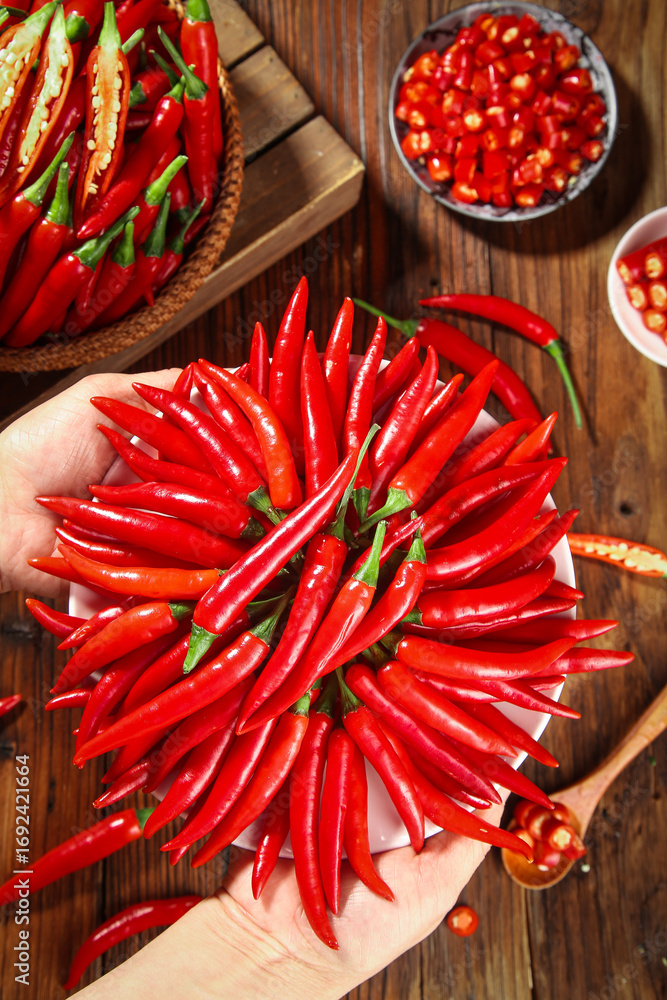 Fototapeta premium Fresh Red Chili Peppers Arranged in Hands on Rustic Wooden Farmhouse Table for Cooking