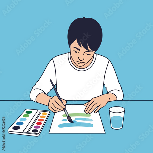 Person painting with watercolors on paper at a table.