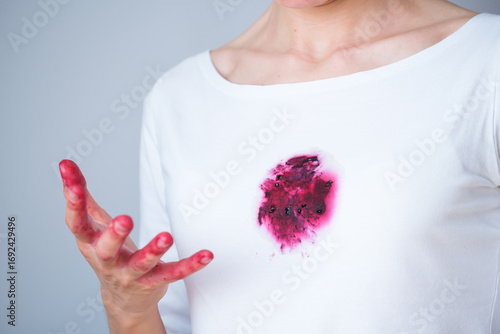 A hand grips ripe blackberries, their juice staining fingertips and a white shirt nearby. The bright setting emphasizes the vibrant berries and the playful mess they create.