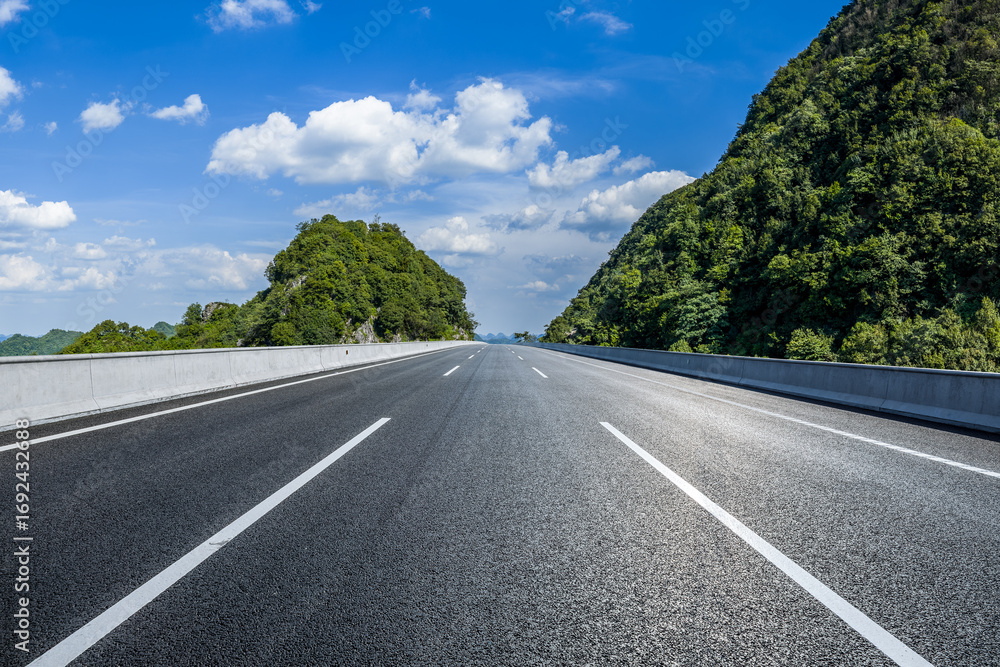 Fototapeta premium Straight asphalt highway road passing through beautiful green mountain natural landscape on a sunny day