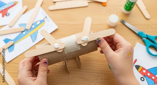Child hands crafting toy airplane from recycled materials on wooden table.