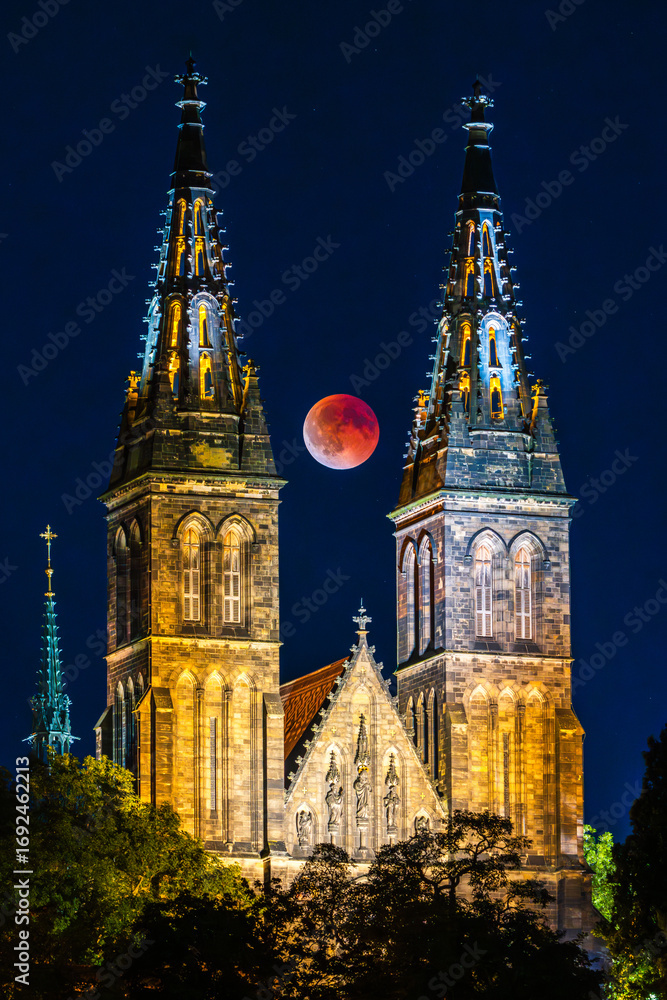 Obraz premium The full Blood Moon during lunar eclipse in between towers of the Vysehrad basilica the UNESCO site in Prague.