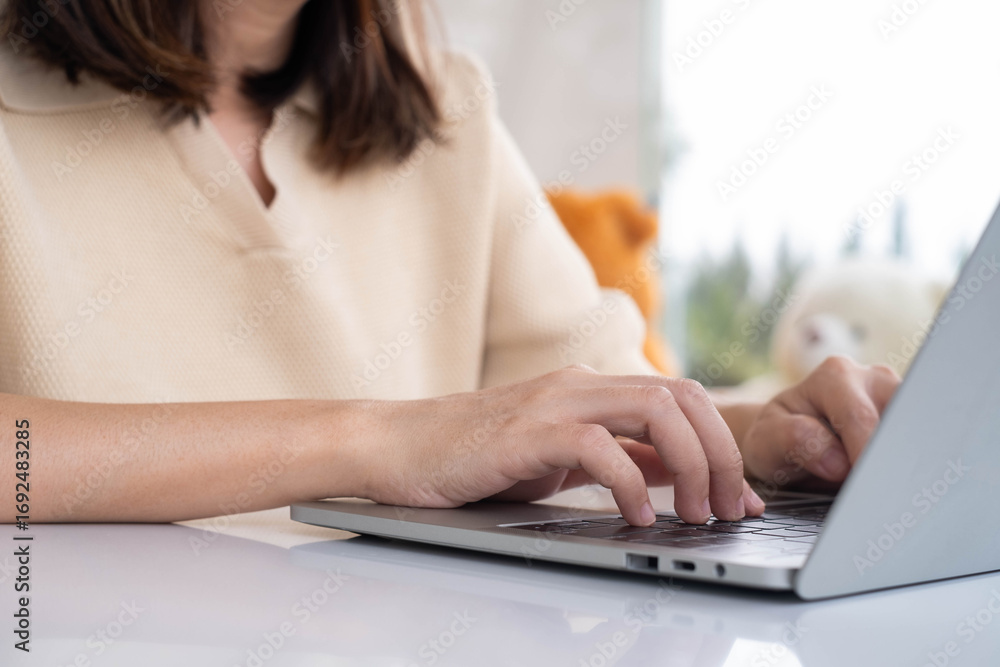 Fototapeta premium Close-up of Asian woman typing on laptop keyboard at home. Concept of remote work, freelancing, online communication, digital workspace, technology usage, or productivity in modern lifestyle.