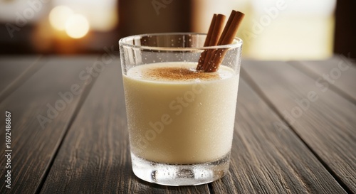 A glass of creamy eggnog with cinnamon sticks on a wooden surface