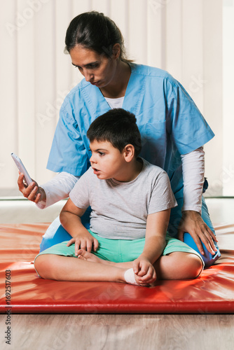 Physiotherapist showing smartphone to child with cerebral palsy during rehabilitation session
