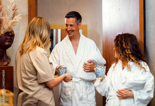 Spa worker offering welcome tea to middle-aged couple entering luxury wellness center.