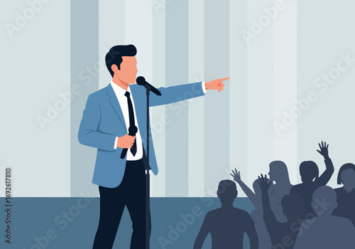 Man speaking into microphone pointing towards audience on stage.