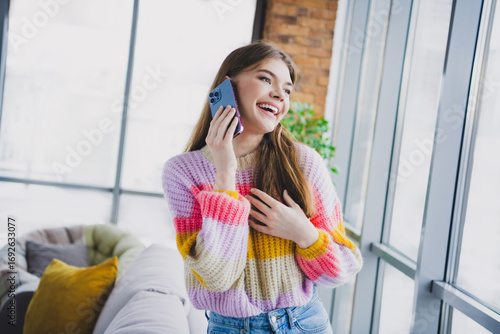 Young woman enjoying a cheerful phone call at home in a vibrant cozy sweater near a sunny window Free Download Young woman enjoying a cheerful phone call at home in a vibrant cozy sweater near a sunny window - GFXLoad