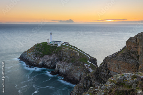 South Stack Lighthouse auf der Insel Holyhead vor der Insel Anglesey an der Küste von Wales bei Sonnenuntergang mit Irland im Hintergrund