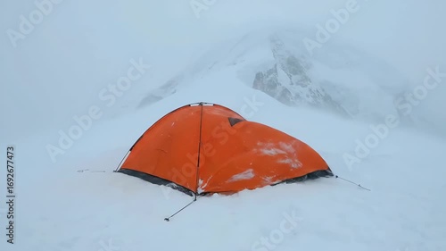 Solitary Orange Tent Bravely Faces a Whiteout Blizzard in the High Mountains, Orange tent standing solitary in a frigid, snow-covered mountain landscape