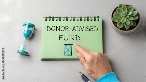 Green notebook with DONOR-ADVISED FUND text and hourglass illustration on gray surface – Charitable giving and timed philanthropy, business, finance, abstract, donation, nonprofit