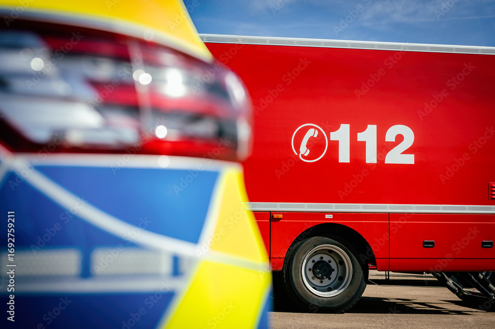 Photos Feuerwehrfahrzeug mit der Notrufnummer 112, daneben ein Polizeiauto im Anschnitt