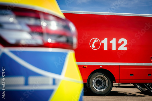 Feuerwehrfahrzeug mit der Notrufnummer 112, daneben ein Polizeiauto im Anschnitt. Symbolisiert Notruf, Einsatzkräfte, Rettungsdienst und öffentliche Sicherheit.