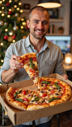 Man holding slice of festive Christmas pizza with red and green toppings in decorated office