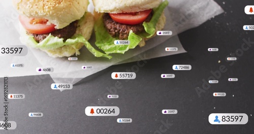 Showcasing slider burgers with sesame buns, lettuce, tomato on dark table with social overlay icons