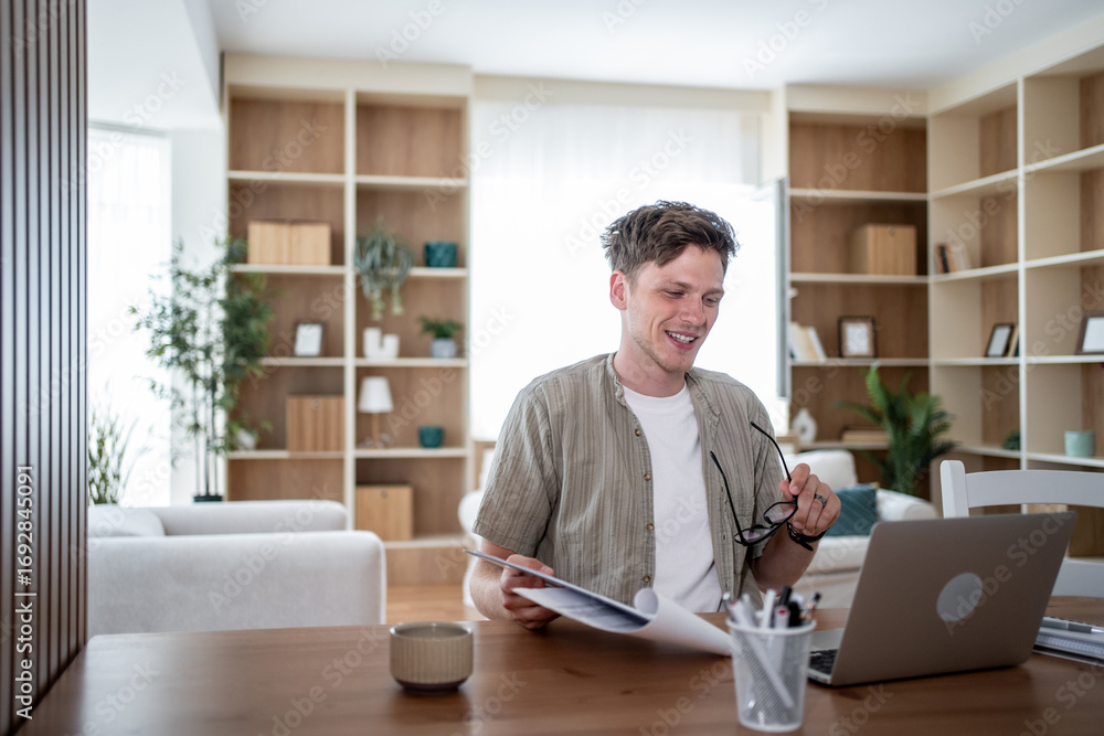 Fototapeta premium Freelancer smiling and working from home using laptop and reading documents