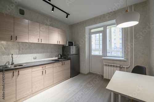 bright, modern kitchen features light wood cabinets, gray countertops, and stainless steel appliances. A balcony door and window provide ample light