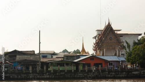 On the Chao Phraya River pier in a neighborhood of Bangkok, Thailand, the Tai pagoda with golden details stands out among the condominiums