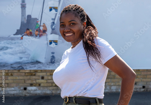 Cowes Isle of Wight England UK. 11.08.2025. An attractive African woman wearing a white tee shirt against a sailing background.