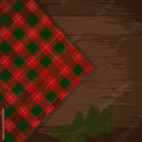 Red and green plaid fabric draped on a wooden surface with a sprig of pine. Christmas themed fabric display with rustic background.