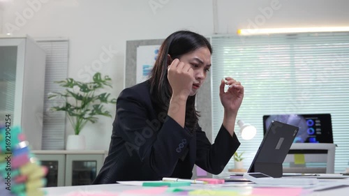 Asian businesswoman suffering from headache and stress while working on a tablet in the office