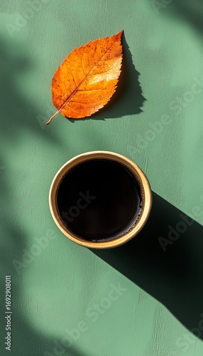 Warm Coffee Cup Beside Autumn Leaf on a Green Surface in Soft Morning Light