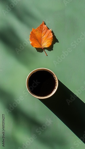 Warm Coffee Cup Beside Autumn Leaf on a Green Surface in Soft Morning Light.