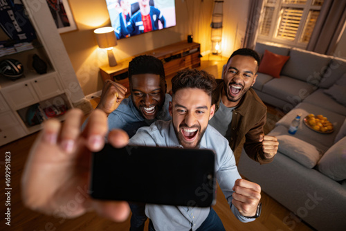 Excited male friends taking selfie while watching sports on tv