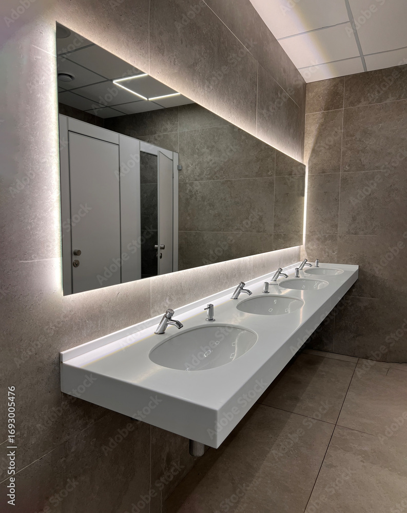Fototapeta premium Modern restroom interior with stone gray tiles. Contemporary interior of public toilet. minimal interior with white tiles, round mirrors. Perspective of men's restroom. commercial bathroom. 