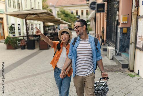 Smiling tourists in their forties holding hands and walking through a charming city street, enjoying sightseeing, love, and travel together