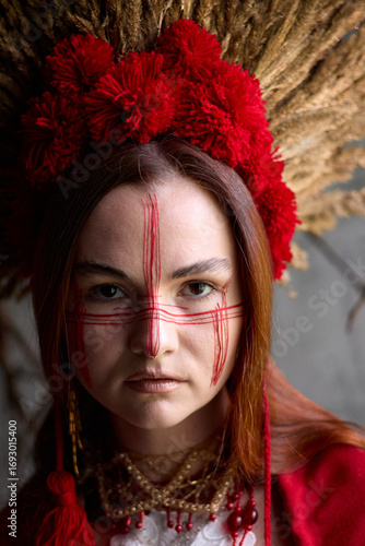 Mysterious woman with red face paint and a traditional headdress poses against a textured background, creating a striking and culturally rich portrait.