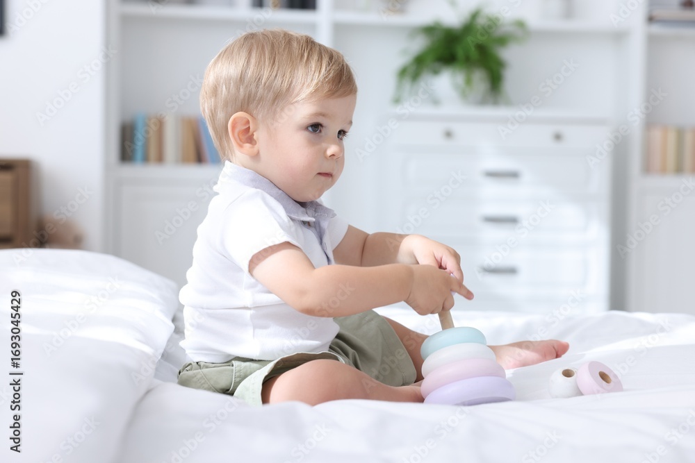 Fototapeta premium Cute little baby playing with toy pyramid on bed at home