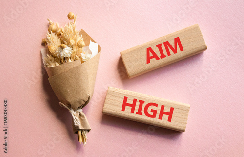 Aim High symbol. Wooden blocks with words Aim High. Beautiful pink background with bouquet of flowers. Business and Aim High concept. Copy space.