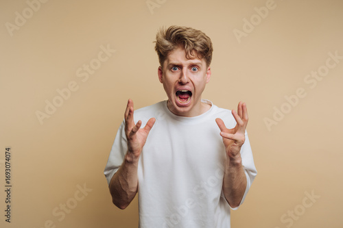 Person expresses intense frustration with raised hands in front of a light beige background during a candid moment