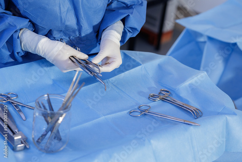 Gloved hands sorting surgical instruments on blue sterile field