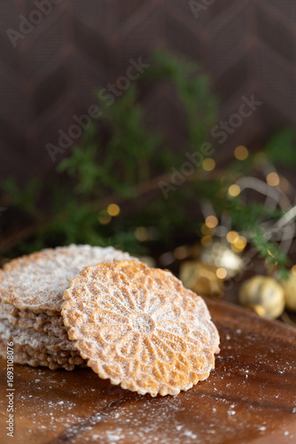 Pizzelles Sprinkled with Powdered Sugar on a Wood Tray with Christmas Decor in Background