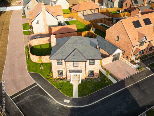 Drone view of a newly completed, detached family home seen on an imposing corner plot location. Smaller homes are in the background of this British housing development site.