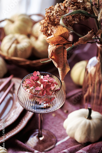 Fotografie A cozy Thanksgiving tablescape with white pumpkins, a glass goblet with pink flo