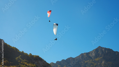 High Altitude Paragliding. Paragliders over rocky mountain peaks against a blue sky.