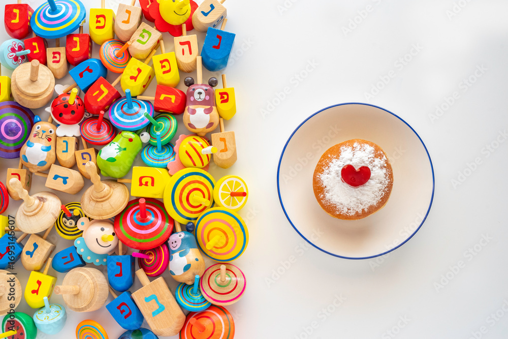 Obraz premium Hanukkah dreidels and traditional donut Sufganiyah for Jewish holiday on white background. Hebrew letters on dreidels say: 