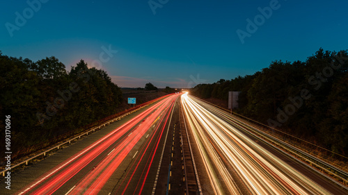 Tableau sur toile Light trails illuminating highway at dusk with moon in the background
