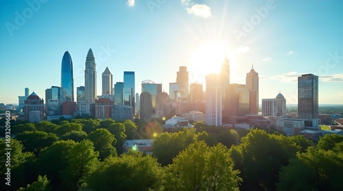 Fototapeta Naklejka Na Ścianę i Meble -  Stunning Charlotte North Carolina city skyline with towering modern skyscrapers, lush green park trees, and bright morning sun in a clear blue sky.